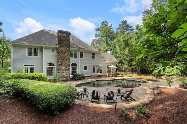 back of house with a chimney, a patio area, an outdoor pool, and roof with shingles