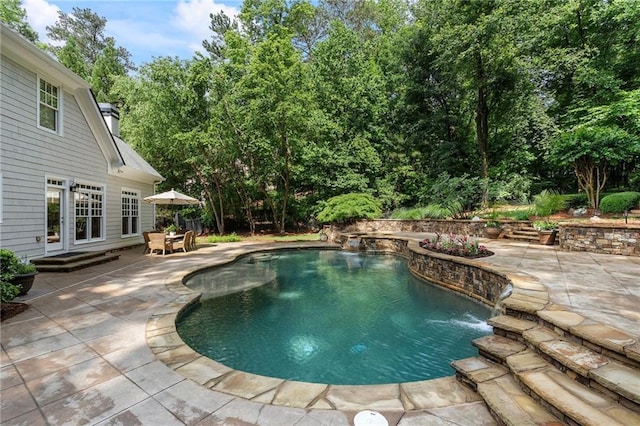 swimming pool with a patio area and view of wooded area