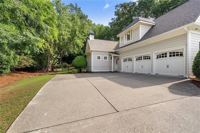 view of side of home with concrete driveway, a shingled roof, a chimney, and a garage