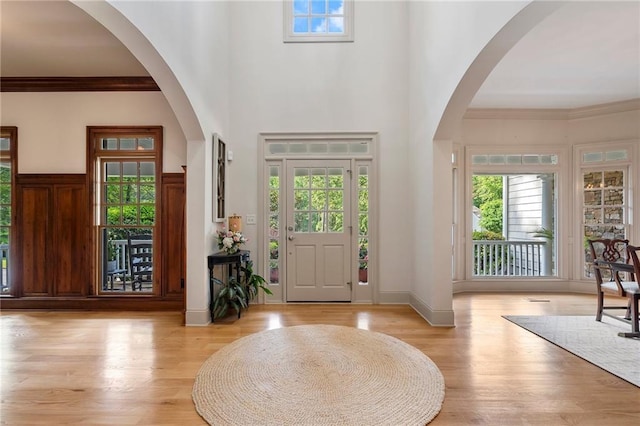 foyer entrance with light wood-style flooring, ornamental molding, and a towering ceiling