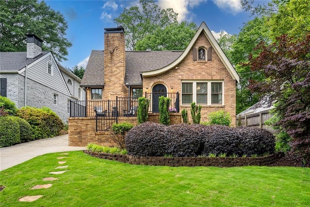 tudor home featuring a shingled roof, a chimney, a front lawn, and brick siding