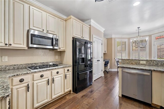 kitchen with ornamental molding, stainless steel appliances, dark wood-type flooring, cream cabinetry, and a notable chandelier