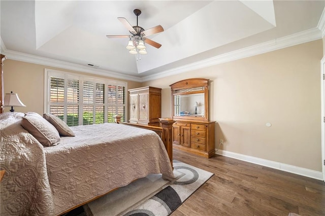 bedroom with baseboards, ornamental molding, wood finished floors, and a raised ceiling
