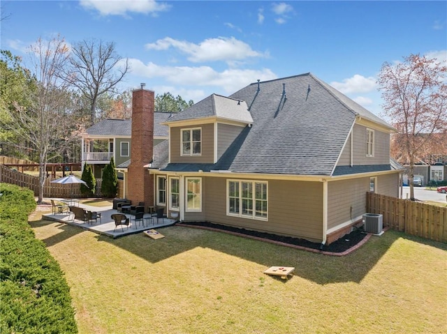 rear view of house with cooling unit, fence private yard, roof with shingles, and a lawn