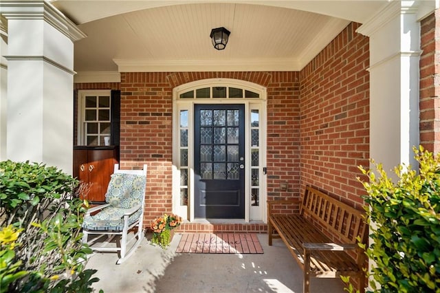 doorway to property featuring covered porch and brick siding