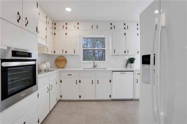 kitchen featuring light countertops, decorative backsplash, white cabinetry, a sink, and white appliances