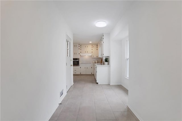 hall with light tile patterned floors, a sink, visible vents, and baseboards