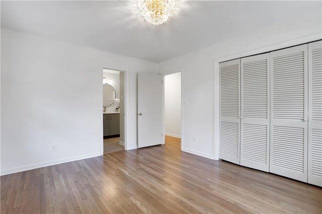 unfurnished bedroom featuring ensuite bath, baseboards, a closet, and wood finished floors