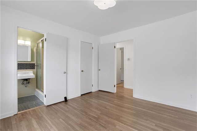 unfurnished bedroom featuring ensuite bath, baseboards, and wood finished floors