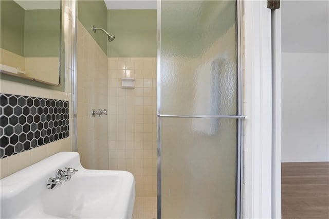 bathroom with tile walls, a sink, a shower stall, and wood finished floors