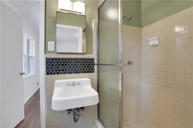 full bath with a stall shower, a sink, tile walls, and wood finished floors