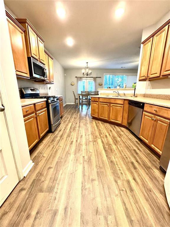 kitchen with kitchen peninsula, appliances with stainless steel finishes, light hardwood / wood-style floors, and a notable chandelier