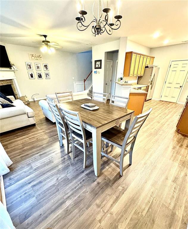 dining room with a stone fireplace, light hardwood / wood-style floors, and ceiling fan with notable chandelier