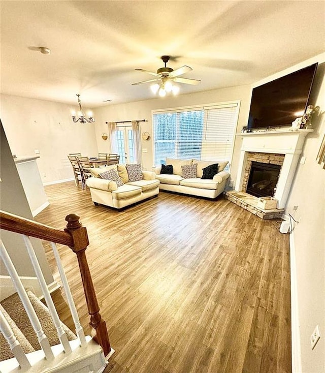 unfurnished living room featuring hardwood / wood-style floors, ceiling fan with notable chandelier, and a stone fireplace