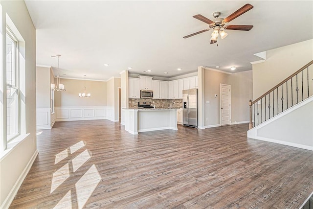 unfurnished living room featuring wood finished floors, ceiling fan with notable chandelier, stairway, ornamental molding, and recessed lighting