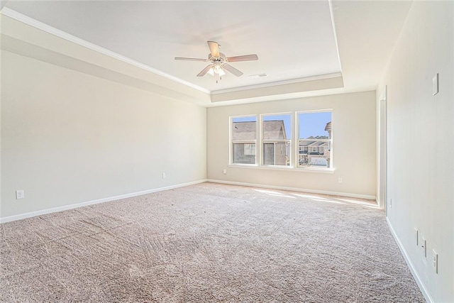 carpeted spare room featuring a ceiling fan, a raised ceiling, ornamental molding, and baseboards