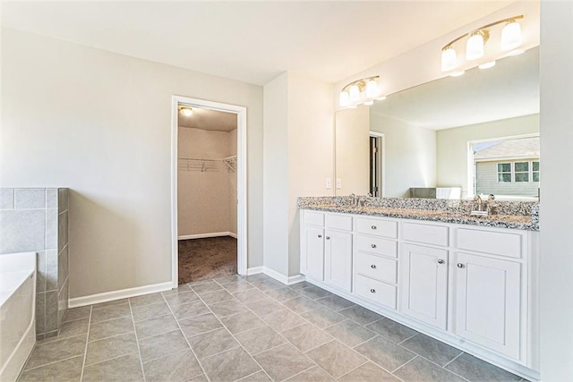 bathroom with a sink, double vanity, a walk in closet, and baseboards