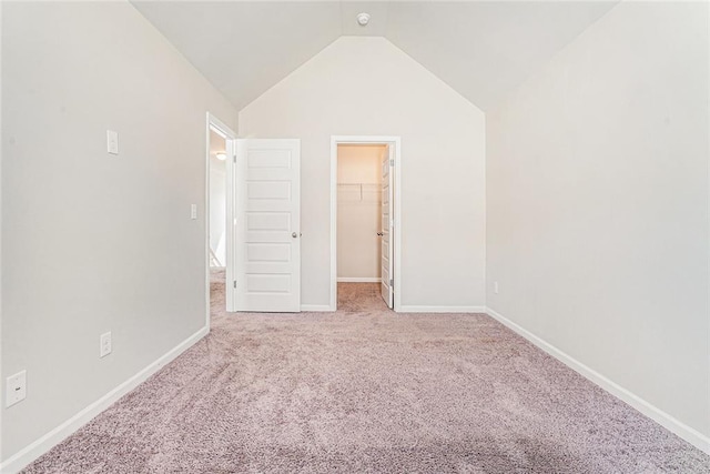 unfurnished bedroom featuring baseboards, carpet flooring, a walk in closet, and vaulted ceiling