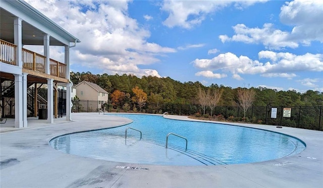 community pool featuring a patio, a forest view, and fence