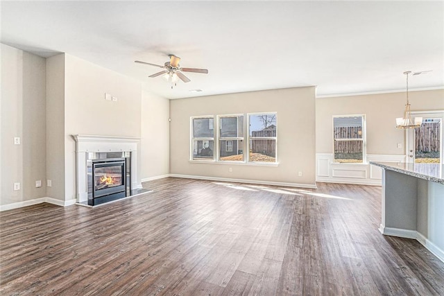 unfurnished living room featuring dark wood-style flooring, ceiling fan with notable chandelier, baseboards, and a glass covered fireplace