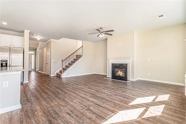 unfurnished living room featuring a ceiling fan, a fireplace, stairway, baseboards, and dark wood-type flooring