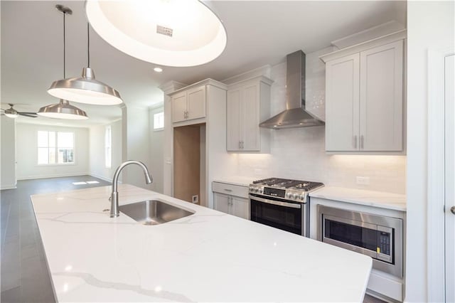 kitchen with stainless steel appliances, wall chimney range hood, light stone countertops, pendant lighting, and sink