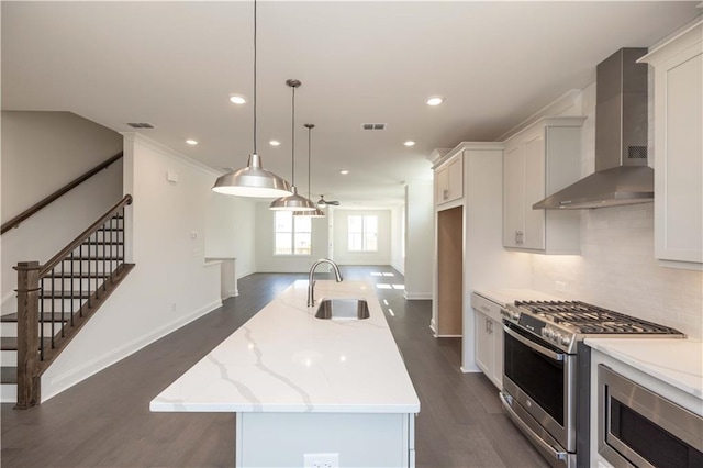 kitchen with stainless steel appliances, a kitchen island with sink, hanging light fixtures, wall chimney range hood, and sink