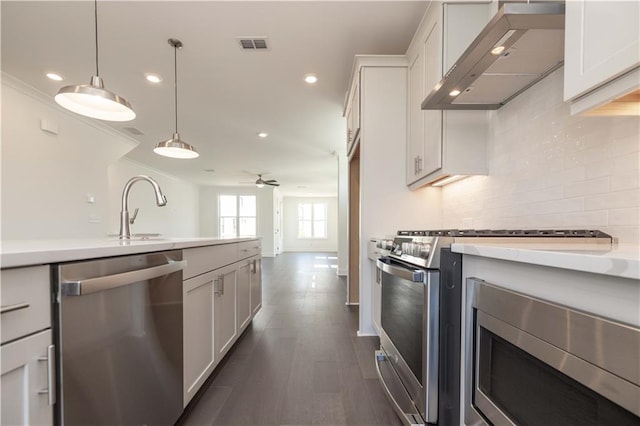 kitchen with appliances with stainless steel finishes, white cabinetry, wall chimney range hood, tasteful backsplash, and ceiling fan