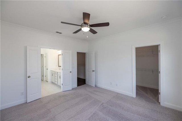 unfurnished bedroom with ceiling fan, crown molding, light carpet, a walk in closet, and a closet