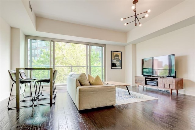 living room featuring dark wood-type flooring, a tray ceiling, and an inviting chandelier