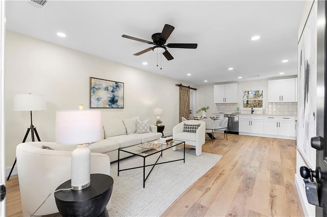 living room featuring sink, light wood-type flooring, ceiling fan, and a barn door