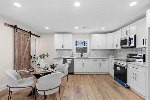 kitchen featuring tasteful backsplash, a barn door, white cabinets, sink, and stainless steel appliances