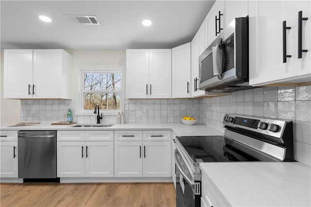 kitchen with appliances with stainless steel finishes, white cabinetry, tasteful backsplash, light hardwood / wood-style floors, and sink