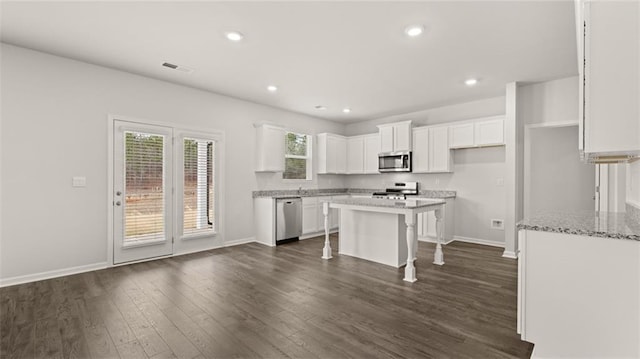 kitchen featuring dark wood-type flooring, appliances with stainless steel finishes, a kitchen island, a kitchen bar, and white cabinetry