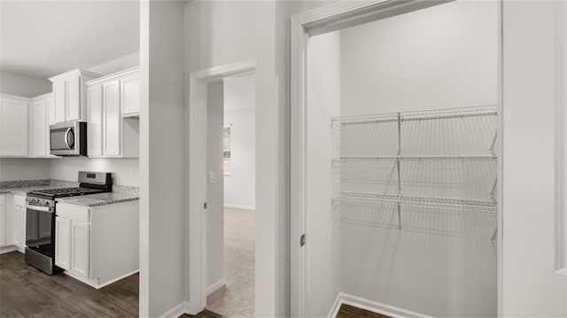 kitchen with light stone countertops, white cabinetry, stainless steel appliances, and dark hardwood / wood-style floors