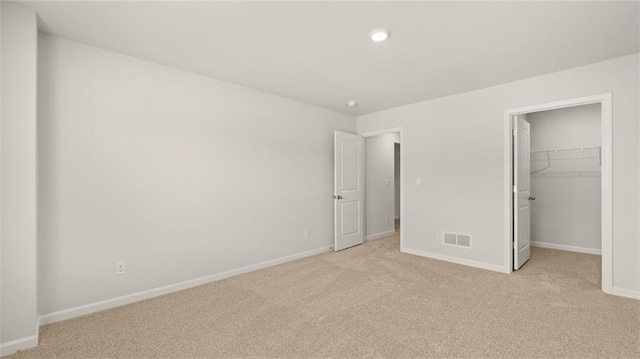 unfurnished bedroom with light colored carpet, a walk in closet, and a closet