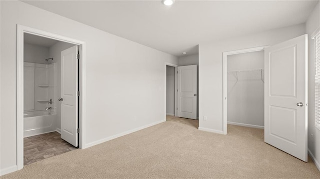 unfurnished bedroom with ensuite bathroom, light colored carpet, and a spacious closet