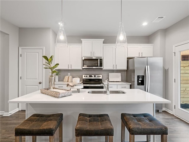 kitchen featuring appliances with stainless steel finishes, dark hardwood / wood-style flooring, sink, a center island with sink, and hanging light fixtures