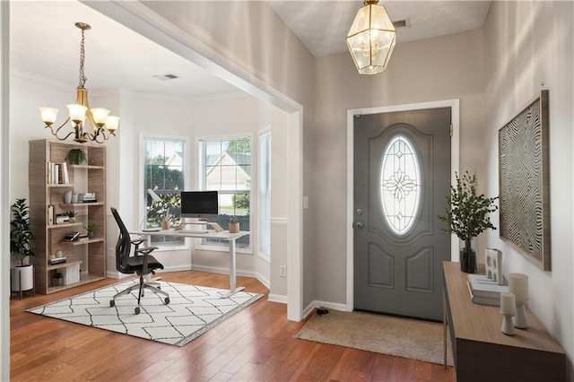 foyer with baseboards, wood-type flooring, visible vents, and a chandelier