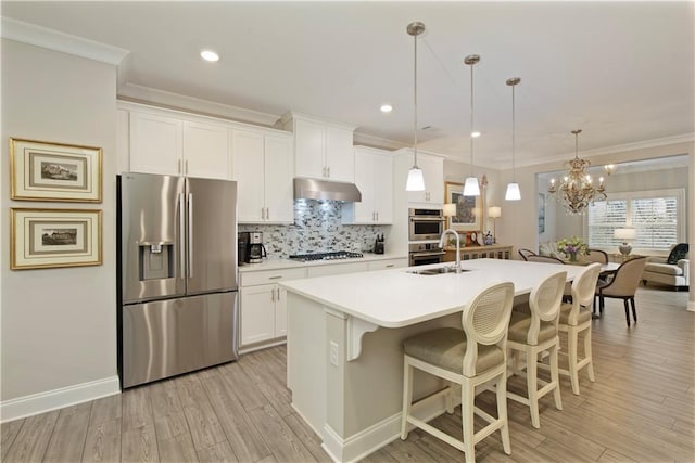 kitchen featuring appliances with stainless steel finishes, ornamental molding, under cabinet range hood, and a kitchen bar