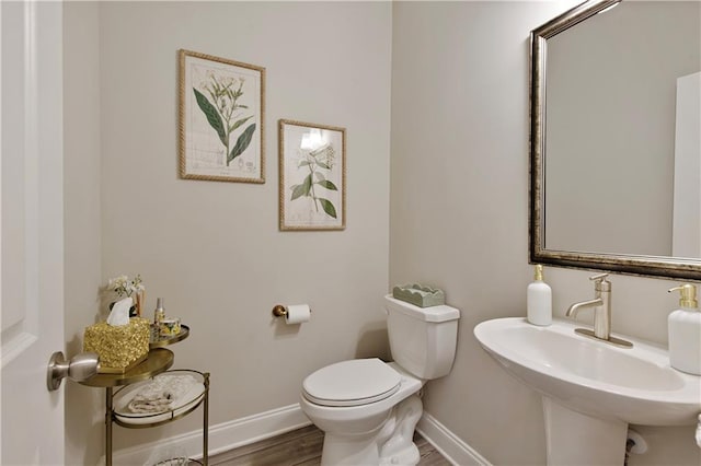 bathroom featuring toilet, baseboards, a sink, and wood finished floors