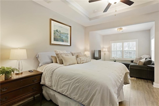 bedroom featuring ceiling fan, ornamental molding, a raised ceiling, and light wood-style flooring