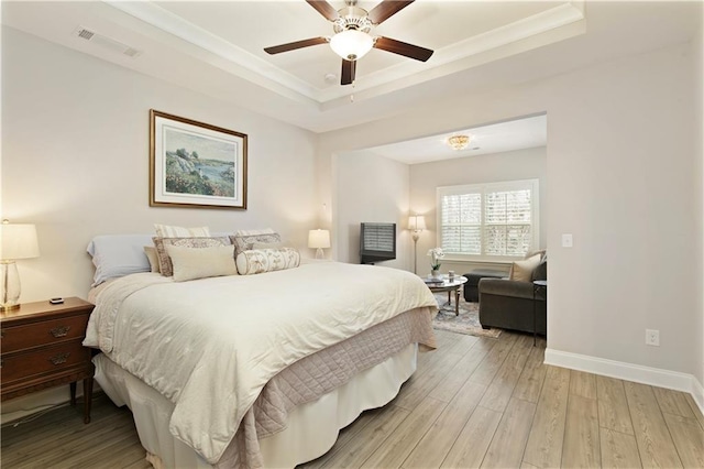 bedroom featuring baseboards, visible vents, ornamental molding, a tray ceiling, and light wood-type flooring