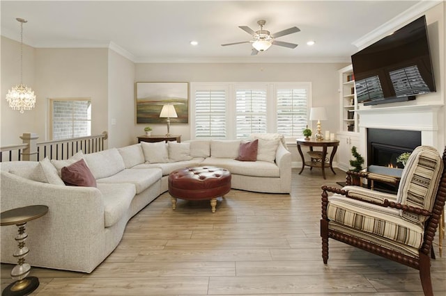 living area with recessed lighting, ceiling fan with notable chandelier, a lit fireplace, light wood finished floors, and crown molding