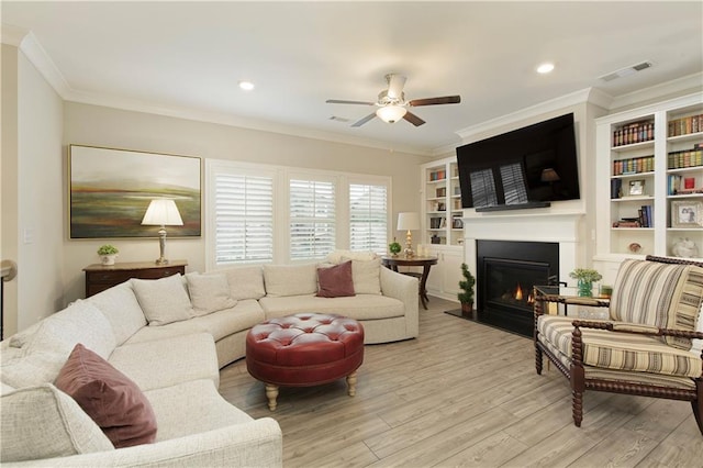 living area with a warm lit fireplace, visible vents, a ceiling fan, ornamental molding, and light wood-type flooring