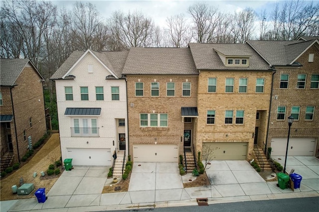 townhome / multi-family property featuring brick siding, a shingled roof, an attached garage, driveway, and stairs