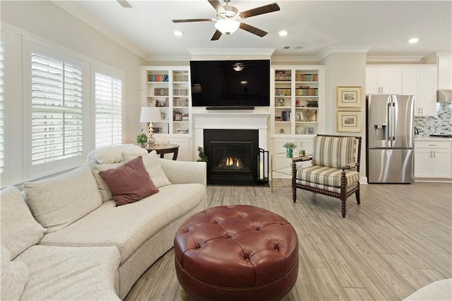 living room featuring light wood finished floors, a fireplace with flush hearth, ceiling fan, ornamental molding, and recessed lighting