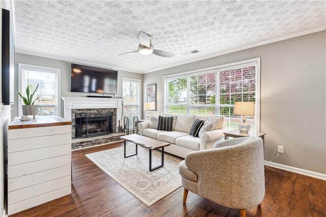 8450 Jot Em Down Rd, Gainesville, GA 30506 - living room featuring a ceiling fan, crown molding, visible vents, a stone fireplace, and dark wood-style floors
