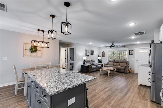 kitchen featuring a kitchen island, hanging light fixtures, stainless steel fridge, ceiling fan, and a breakfast bar area