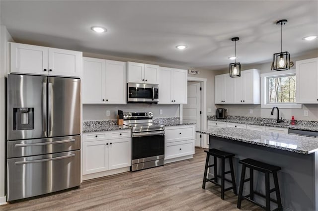 kitchen featuring pendant lighting, a center island, white cabinetry, light stone countertops, and appliances with stainless steel finishes